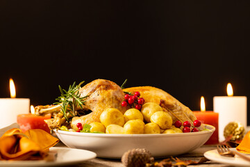 Thanksgiving table with roast chicken, vegetables, candles and autumn decoration