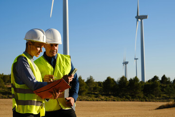 Two engineers checking data on the mobile phone while working in a wind turbine field.