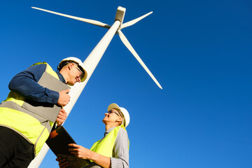 Low angle view of two workers smiling while working together in a wind turbine field.