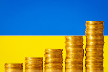 Stacks of golden coins forming upward graph on background of flag of Ukraine. Financial development of Ukraine after the war concept