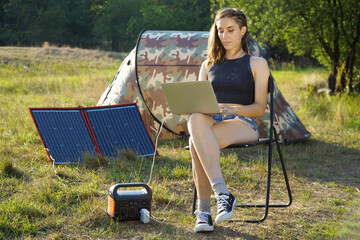 Woman uses solar panel and power station to generate electricity for working on laptop 