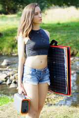 Woman outdoors in nature carries solar panel and power station for independent power supply