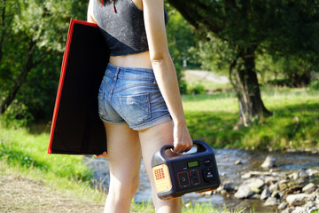 Woman out in nature carries solar panel and power station for independent power supply