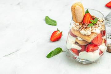 Traditional Italian dessert tiramisu with fresh strawberry, mascarpone and mint in glass on light background. Long banner format