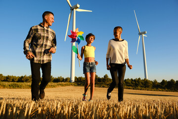 Girl playing with a wind turbine toy while having fun with her parents in wind turbines field.