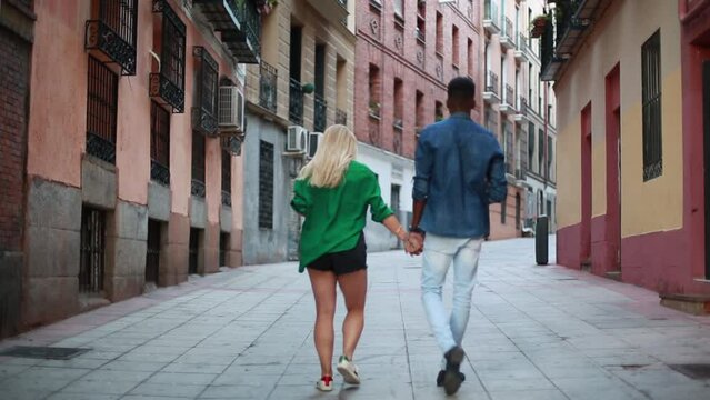 back view Multiethnic couple holding hands while walking along a pedestrian street