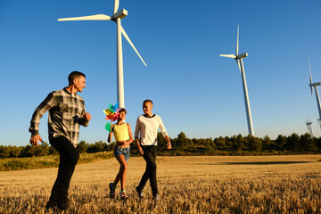 Girl holding a wind turbine toy while enjoy with her parents outdoors in a wind turbine field