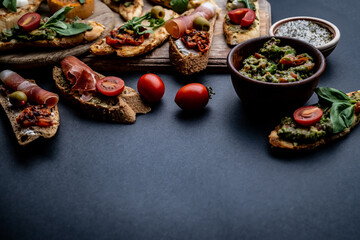 Fototapeta na wymiar Set of bruschettas with jamon, olives, pesto, tomatoes, basil and mozzarella served on wooden board with guacamole and cherries. Traditional mediterranean antipasti food composition with copy space