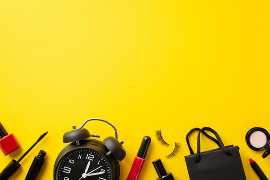 Black Friday Concept. Top View Photo Of Alarm Clock Paper Bag Cosmetics Mascara Eyeshadow Nail Polish False Eyelashes And Lip Gloss On Isolated Yellow Background With Empty Space