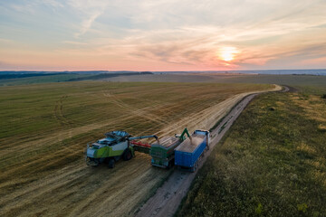 Aerial view of combine harvester unloading grain in cargo trailer working during harvesting season...