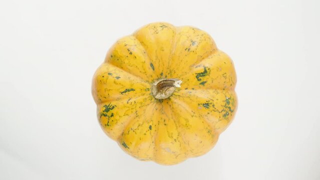 Orange pumpkin with green dots, rotating on a white background, top view.