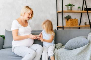 A pregnant young girl is sitting on the sofa with her little daughter and playing on the phones. The concept of the problem of addiction to gadgets in children and adults