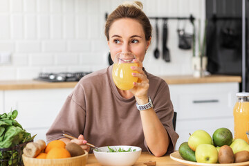 healthy lifestyle. Happy young woman eating salad and drinking orange juice while sitting at home...