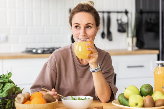 healthy lifestyle. Happy young woman eating salad and drinking orange juice while sitting at home in the kitchen. Young female eat wholesome breakfast