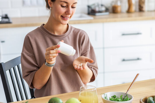 Happy Caucasian woman in home kitchen holding bottle of nutritional supplements, healthy lifestyle