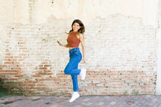 Full Length Of An Excited Young Woman Dancing And Jumping Outside