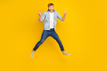 Fototapeta na wymiar Full length photo of impressed handsome guy blue shirt jeans sneakers flying show v-sign scream yeah isolated on yellow color background