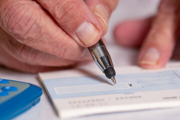 A male hand is filling out the amount in pound sterling on a blank cheque. Writing a check.