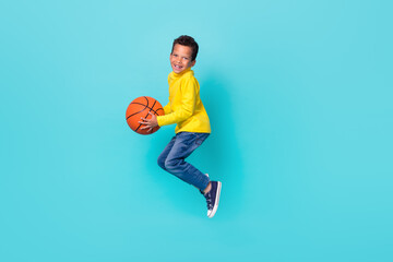 Full size portrait of energetic overjoyed boy jumping arms hold basketball have good mood isolated on cyan color background