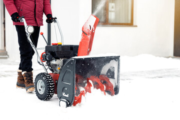 Closeup of red snow blower in action. Senior mature man outdoor in front of house using snowblower...