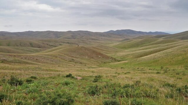 Vast hilly landscape in the Mongolian steppe. Pan view footage over the horizon over land. Unpaved road through the endless vast steppe of central Mongolia. Far horizon over land. Adventure travel
