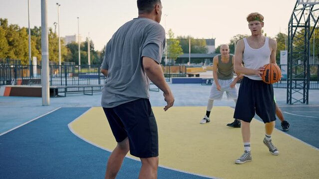 Sportive men compete playing streetball on outdoor court