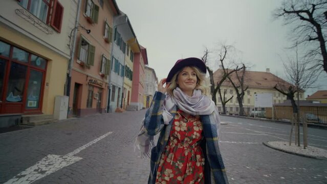Young female tourist admiring old city buildings dressed in warm coat and hat. Woman accomplishes her wish on visiting an old city downtown. The concept of tourism, youth, ancient architecture.