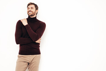 Fototapeta premium Portrait of handsome smiling stylish hipster lambersexual model. Sexy man dressed in turtleneck sweater and trousers. Fashion male isolated on white wall in studio