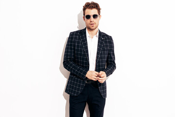 Portrait of handsome confident stylish hipster lambersexual model. Sexy modern man dressed in black elegant suit. Fashion male posing in studio near white wall. In sunglasses