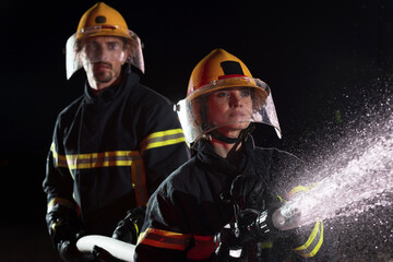 Fototapeta premium Firefighters using a water hose to eliminate a fire hazard. Team of female and male firemen in dangerous rescue mission. 