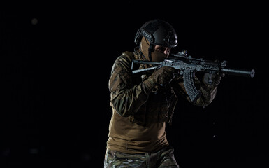 Army soldier in Combat Uniforms with an assault rifle, plate carrier and combat helmet going on a dangerous mission on a rainy night. 