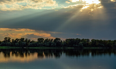The bright rays of the Sun come out of the clouds over the river. Beautiful natural landscape of Ukraine in cloudy weather