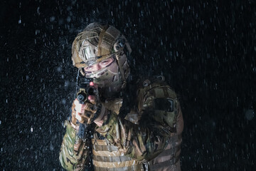 Army soldier in Combat Uniforms with an assault rifle, plate carrier and combat helmet going on a dangerous mission on a rainy night. 