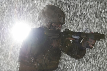 Naklejka premium Army soldier in Combat Uniforms with an assault rifle, plate carrier and combat helmet going on a dangerous mission on a rainy night. 
