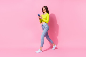 Full length photo of sweet pretty girl dressed lime shirt walking communicating modern device isolated pink color background