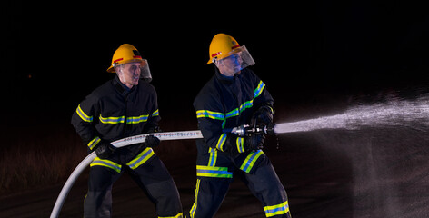 Firefighters use a water hose to eliminate a fire hazard. Team of firemen in the dangerous rescue mission.