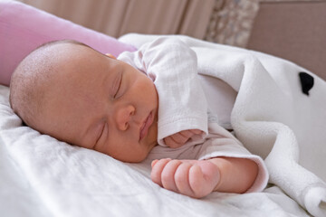 cute little newborn baby girl peacefully sleeps in the nursery on a white cotton bed