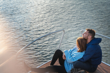 Young romantic hugging couple sitting on the bow of a yacht during sunset. Sea travel and honeymoon concept