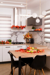 Autumn kitchen interior. Red and yellow leaves and flowers in the vase and pumpkin on light background