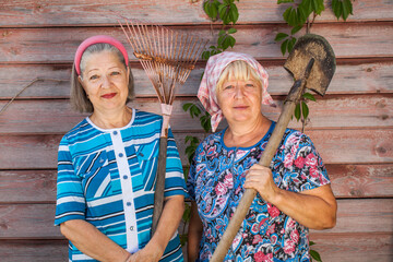 Two elderly women with a garden rake and a shovel