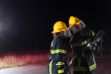 Fototapeta premium Firefighters using a water hose to eliminate a fire hazard. Team of female and male firemen in dangerous rescue mission. 