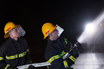 Firefighters use a water hose to eliminate a fire hazard. Team of firemen in the dangerous rescue mission.