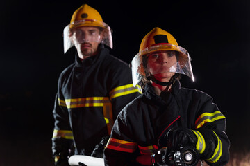 Firefighters using a water hose to eliminate a fire hazard. Team of female and male firemen in...