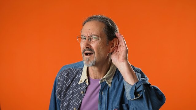 Man struggles to hear, having difficulty hearing, isolated on solid orange background studio portrait.