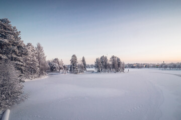 Frosty morning in the Finnish town of Kajaani in the north of the country in the Kainu region. A view of the frozen Kajaaninjoki river and the snowy forest near the river. Sunrise