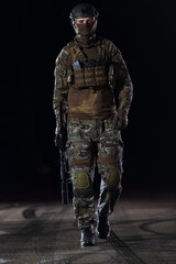 Army soldier in Combat Uniforms with an assault rifle, plate carrier and combat helmet going on a dangerous mission on a rainy night. 