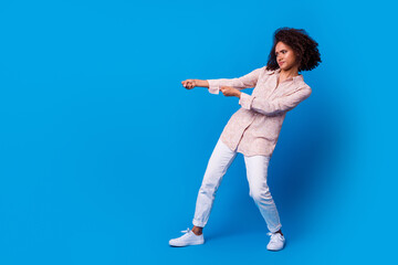 Fototapeta na wymiar Full body portrait of hardworking determined lady arms pull empty space isolated on blue color background
