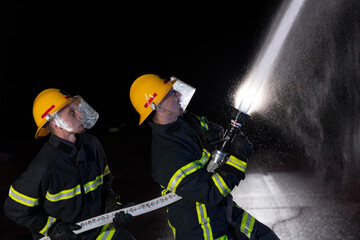 Firefighters use a water hose to eliminate a fire hazard. Team of firemen in the dangerous rescue mission.