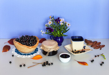 Freshly picked bird cherry berries in wooden bowl and delicious fragrant pitted jam in jar near cup...