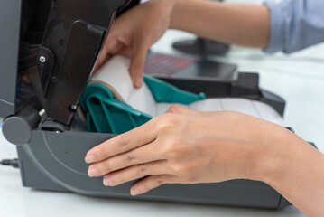 Asian woman inserts a barcode sticker into a barcode printer.